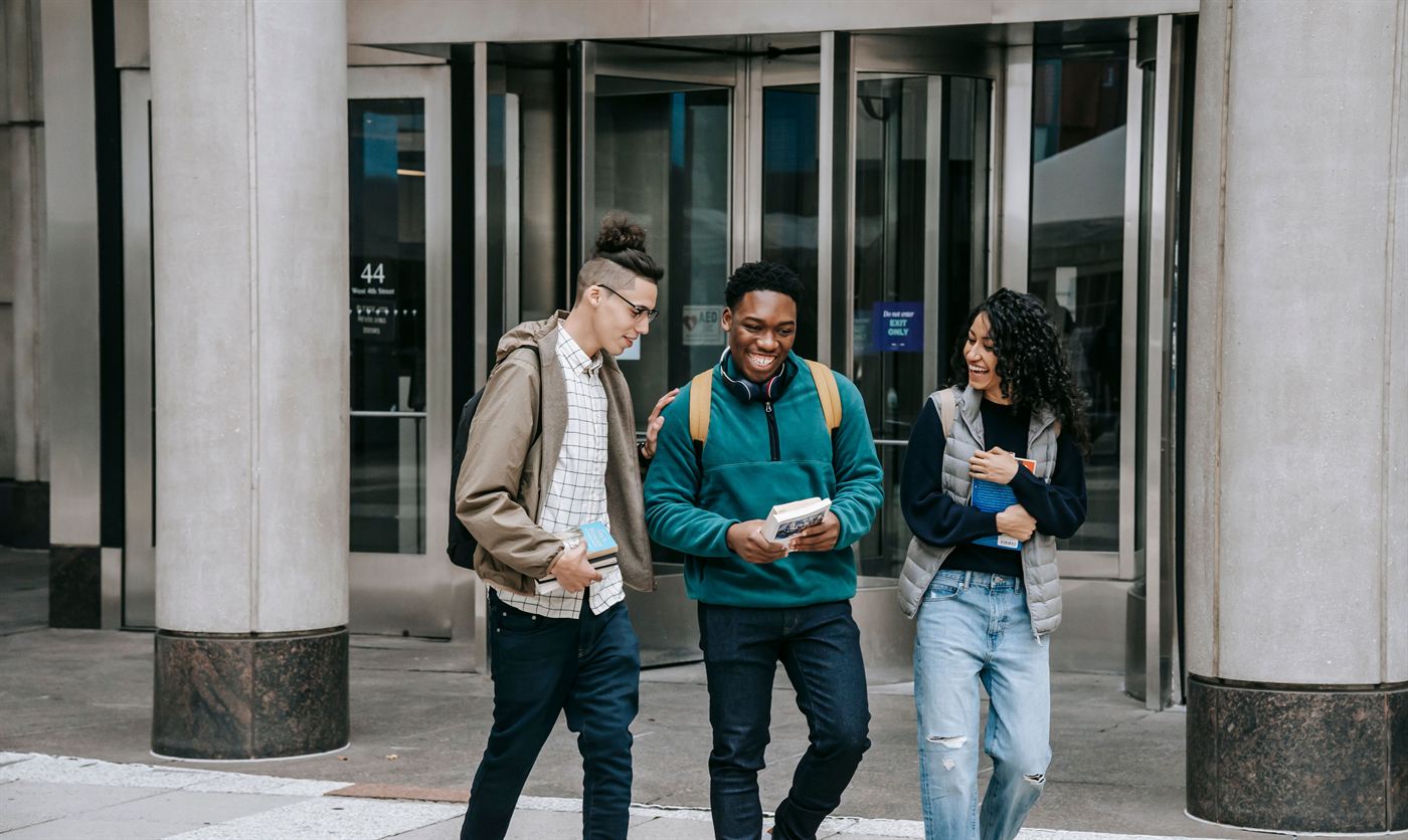 Three young adults holding books outside a building